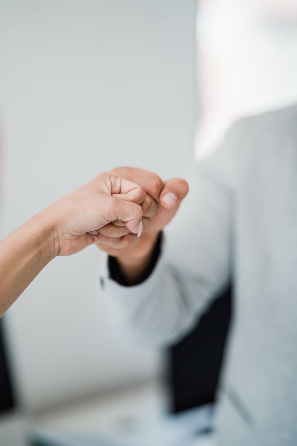 Close-up of two professionals bumping fists, symbolizing teamwork and respect in a modern office.